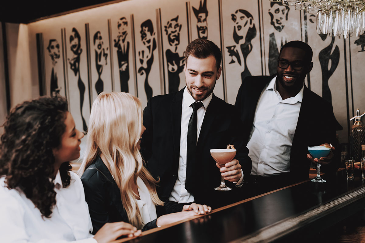 two men approaching two women at bar